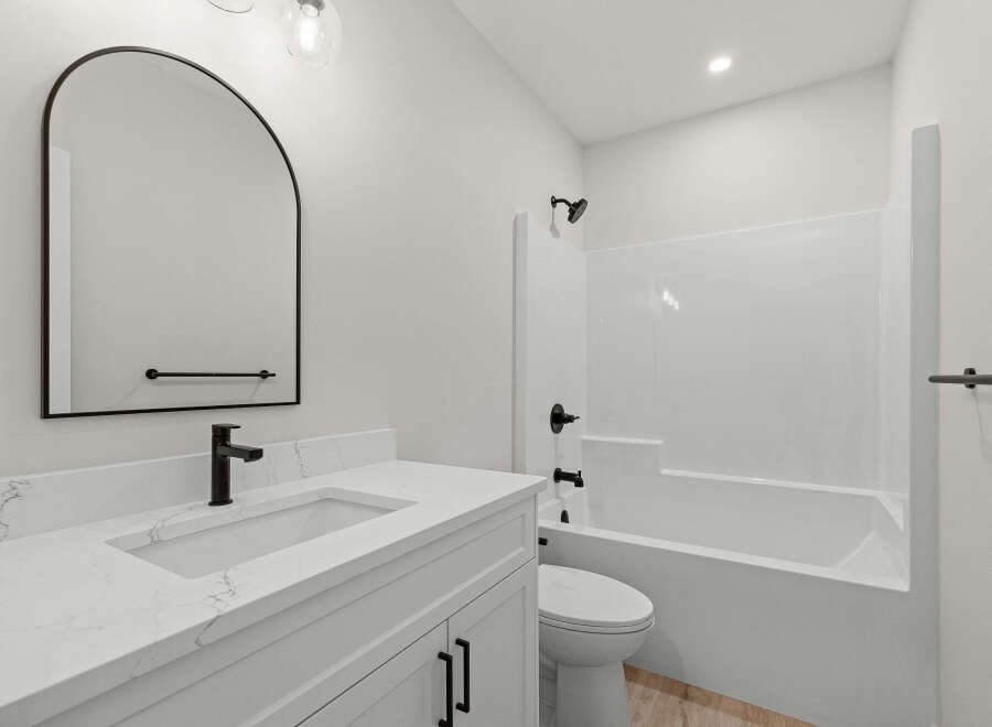This modern bathroom features a sleek vanity with a quartz countertop and a black faucet, complemented by a large arched mirror.