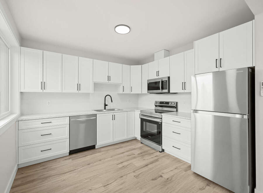 Discover this modern kitchen featuring sleek white cabinetry and stainless steel appliances, including a refrigerator, microwave, and oven.