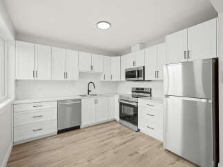 Discover this modern kitchen featuring sleek white cabinetry and stainless steel appliances, including a refrigerator, microwave, and oven.