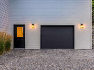 This modern home features a sleek dark garage door and a welcoming black entry door with a glass pane, illuminated by stylish outdoor lighting.