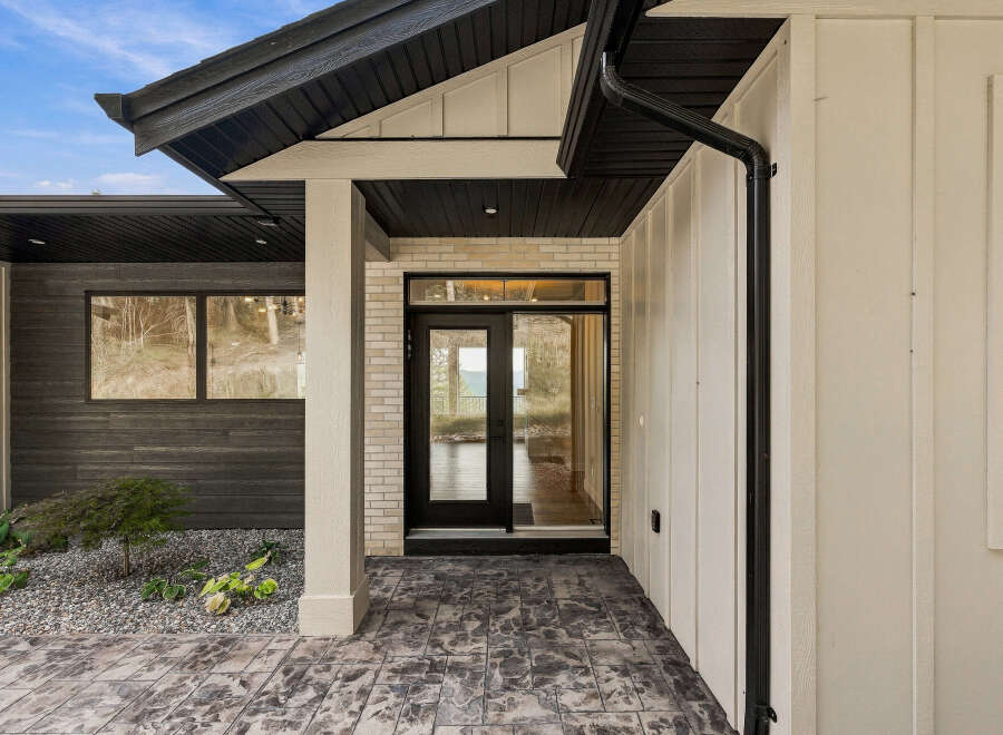 Experience modern living with this stunning home featuring a sleek entryway with a glass-paneled door and large windows.