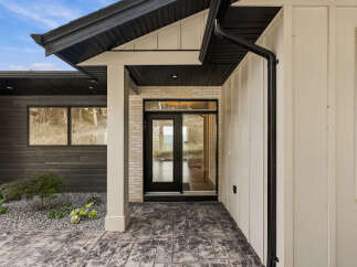 Experience modern living with this stunning home featuring a sleek entryway with a glass-paneled door and large windows.