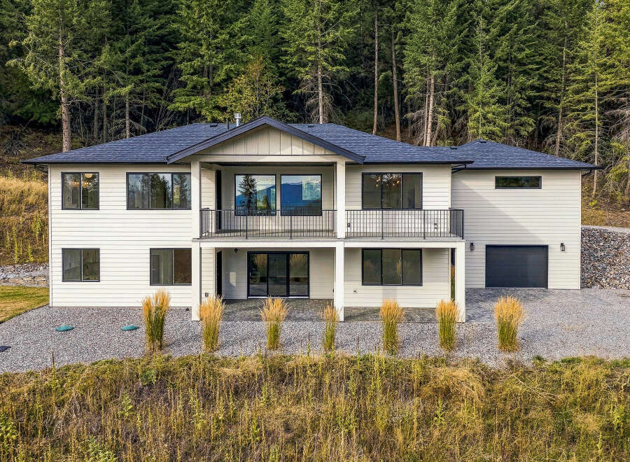 This modern two-story home boasts a sleek white exterior set against a backdrop of lush green pine trees.