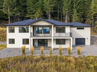 This modern two-story home boasts a sleek white exterior set against a backdrop of lush green pine trees.