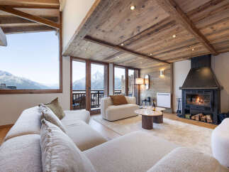 Experience luxury mountain living in this stunning chalet living room, featuring a cozy fireplace and breathtaking panoramic views of snow-capped peaks through expansive windows.