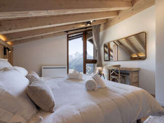 Experience breathtaking mountain views from this charming attic bedroom, featuring a cozy bed adorned with plush white linens and decorative pillows.