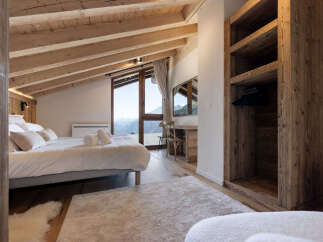 Experience breathtaking mountain views from this charming attic bedroom, featuring a cozy bed and a rustic wooden wardrobe.