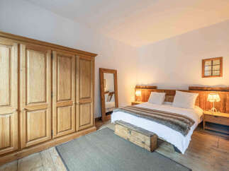 Experience rustic charm in this inviting bedroom, featuring a spacious wooden wardrobe and a cozy bed adorned with a plush throw.