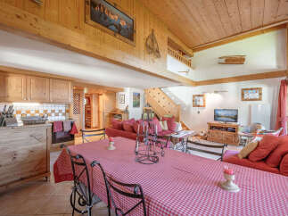 Experience rustic charm in this spacious mountain chalet, featuring a fully equipped wooden kitchen and a cozy living area with a large red-checked dining table.