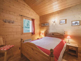 Experience rustic charm in this cozy wooden cabin bedroom, featuring a comfortable bed adorned with a red and white quilt.
