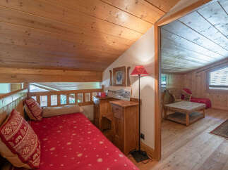 Experience cozy alpine living in this charming bedroom featuring a rustic wooden interior and a comfortable red-covered bed adorned with decorative pillows.
