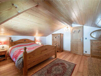 Experience rustic charm in this cozy attic bedroom, featuring a beautiful wooden bed adorned with a patterned quilt.