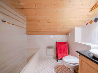 This charming bathroom features a cozy wooden ceiling and white tiled walls, creating a bright and airy atmosphere.