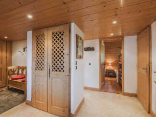 Step into a charming chalet hallway featuring warm wooden ceilings and floors, complemented by elegant lattice-style double doors.
