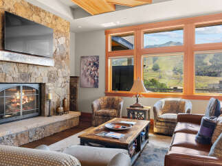 Experience luxury mountain living in this stunning living room, featuring a grand stone fireplace and a large flat-screen TV.