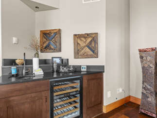 This wet bar area features a sleek black countertop with a built-in sink and modern faucet, complemented by a stainless steel wine fridge.