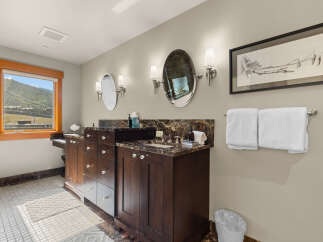 This spacious bathroom features a double vanity with marble countertops and dark wood cabinetry, complemented by elegant sconce lighting and oval mirrors.