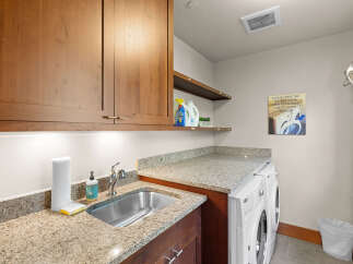 This laundry room boasts ample storage with custom wood cabinetry and a spacious granite countertop.