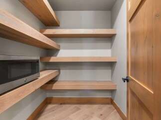 Discover ample storage in this modern pantry, featuring sleek, floating wooden shelves perfect for organizing groceries and appliances.