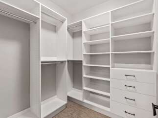 Discover ample storage in this spacious walk-in closet, featuring custom white shelving and drawers.