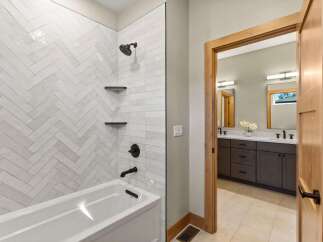 Experience modern luxury in this stunning bathroom featuring a chic herringbone tile shower and a deep soaking tub.
