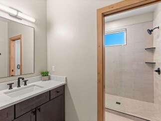 This modern bathroom features a sleek vanity with a white undermount sink and dark wood cabinetry, complemented by a large black-framed mirror and a linear light fixture.
