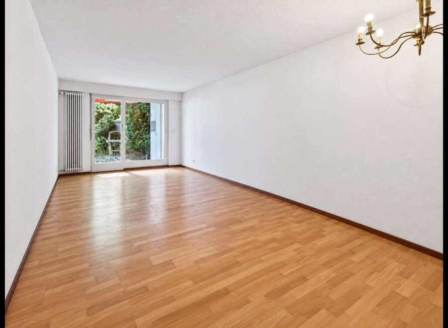 Experience bright and airy living in this spacious room featuring gleaming hardwood floors and large sliding glass doors that open to a lush garden view.
