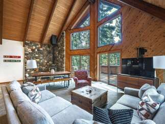 Experience rustic charm in this spacious living area, featuring a soaring wood-paneled A-frame ceiling and a striking stone fireplace.