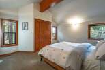 Experience cozy cabin living in this charming bedroom featuring a vaulted ceiling with exposed wooden beams and ample natural light from multiple windows.