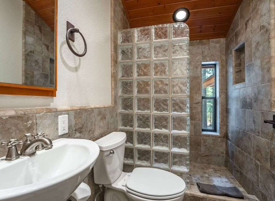 Experience rustic charm in this bathroom featuring a unique glass block shower enclosure and warm wood-paneled ceiling.