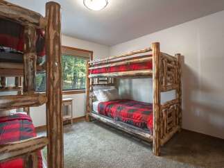 Experience rustic charm in this cozy cabin bedroom featuring sturdy log bunk beds with classic red and black buffalo plaid bedding.