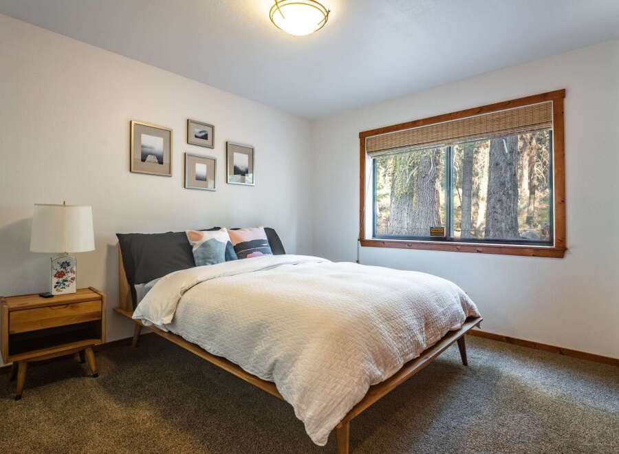 Experience serene forest views from this charming bedroom, featuring a comfortable queen-size bed adorned with plush pillows and a cozy white quilt.