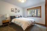 Experience serene forest views from this charming bedroom, featuring a comfortable queen-size bed adorned with plush pillows and a cozy white quilt.