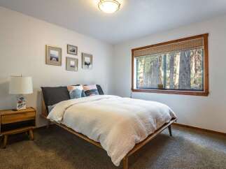 Experience serene forest views from this charming bedroom, featuring a comfortable queen-size bed adorned with plush pillows and a cozy white quilt.
