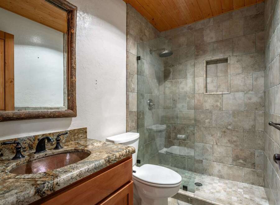 Experience rustic charm in this bathroom featuring a copper vessel sink atop a granite countertop and a wooden vanity.