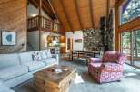 Experience rustic charm in this spacious living area featuring a grand stone fireplace and a soaring vaulted wood-beamed ceiling.