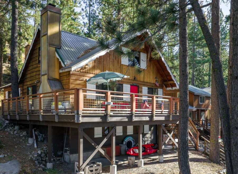 Nestled among tall pine trees, this charming wooden cabin offers a rustic retreat with a spacious deck perfect for outdoor entertaining.