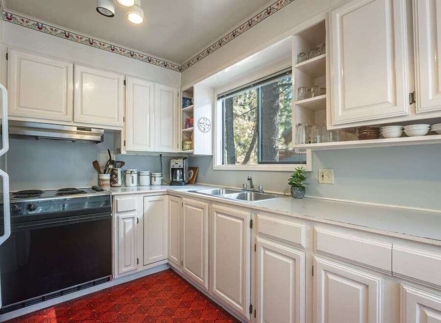 This charming kitchen features crisp white cabinetry and a classic floral wallpaper border, creating a bright and inviting atmosphere.
