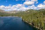 Experience serene lakeside living with this stunning aerial view of a property nestled amongst lush pine forests.