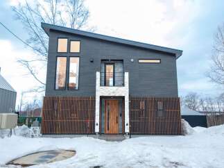 Discover modern living in this striking dark-clad home featuring a unique asymmetrical roofline and large windows that flood the interior with natural light.