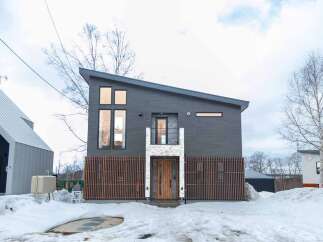 Discover modern living in this striking dark-clad home featuring a unique asymmetrical roofline and a warm wooden door entrance.