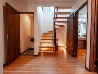 Step into a modern home featuring a sleek wooden staircase bathed in warm light, leading to upper levels.