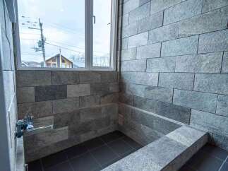 Experience modern luxury in this bathroom featuring sleek, stone-tiled walls and a built-in soaking tub.