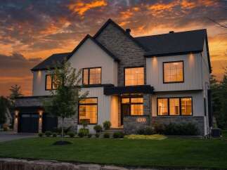 Experience modern luxury in this stunning home featuring a striking stone and white siding exterior, illuminated by a dramatic sunset sky.