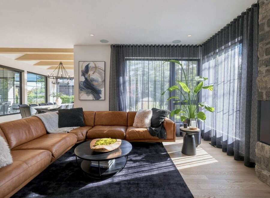 Experience modern luxury in this spacious living room, featuring a plush, cognac leather sectional sofa complemented by a dark, textured rug.