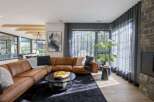 Experience modern luxury in this spacious living room, featuring a plush, cognac leather sectional sofa complemented by a dark, textured rug.