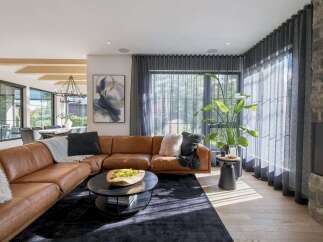 Experience modern luxury in this spacious living room, featuring a plush, cognac leather sectional sofa complemented by a dark, textured rug.
