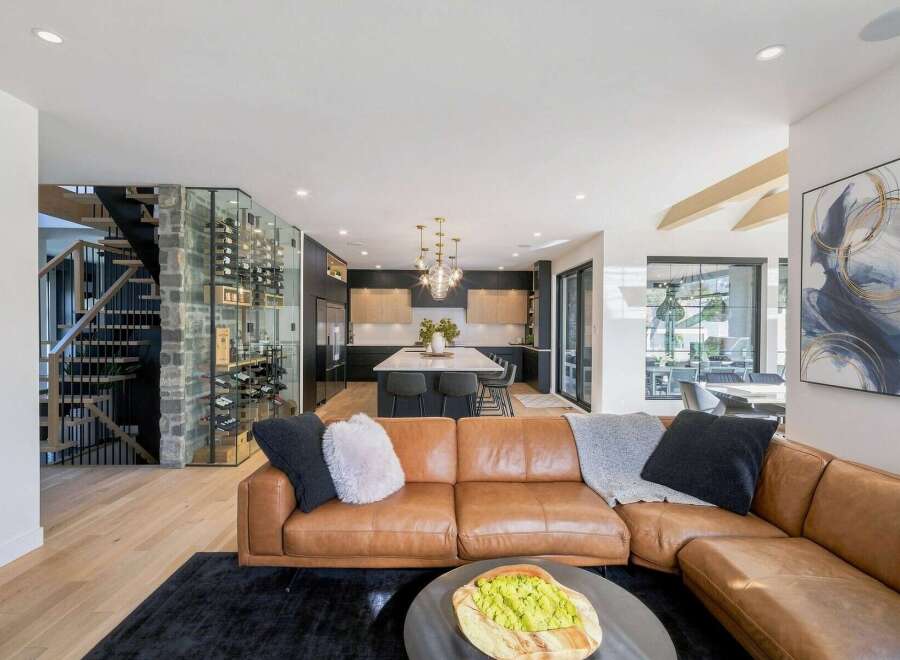 Experience modern luxury in this open-concept living space, featuring a stunning glass-encased wine cellar and a sleek, contemporary kitchen with a large island.