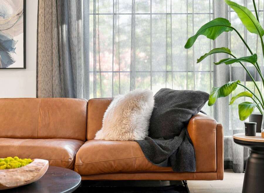 Experience modern comfort in this inviting living space, featuring a luxurious tan leather sofa adorned with plush throw pillows and a cozy blanket.