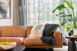 Experience modern comfort in this inviting living space, featuring a luxurious tan leather sofa adorned with plush throw pillows and a cozy blanket.